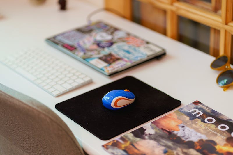 Mini souris d'ordinateur Logitech sur un tapis de souris noir à côté d'un ordinateur portable sur un petit bureau blanc d'un bureau à domicile.
