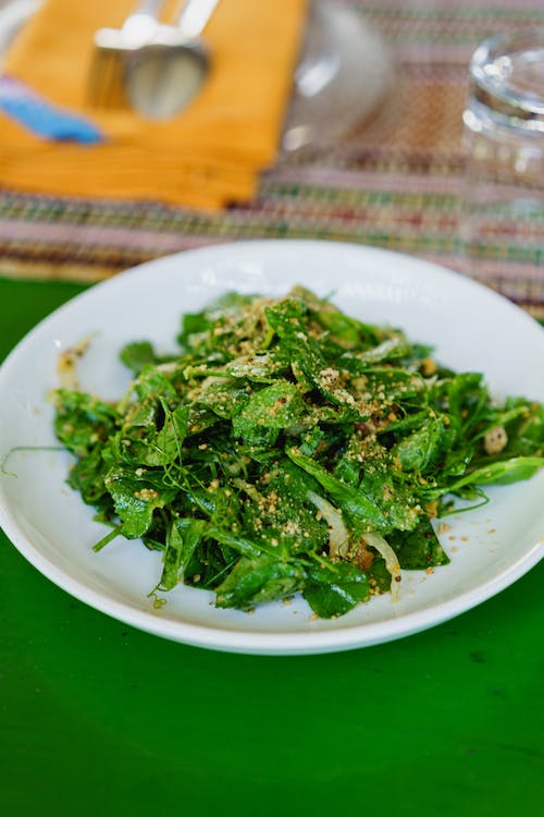 Salade de feuilles de thé birmanes dans une assiette blanche sur une table verte lors d'un cours de cuisine