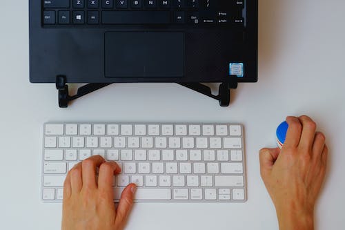 Femme utilisant une petite souris sans fil avec un clavier apple magic et un ordinateur portable sur un support dans un bureau à domicile.