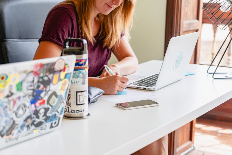 Fille blonde travaillant à distance dans un espace de coworking depuis une table commune partagée à la lumière naturelle.