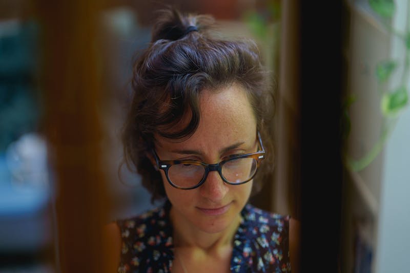 Femme se concentrant sur son travail dans un bureau à domicile vu à travers les vitres d'une fenêtre.