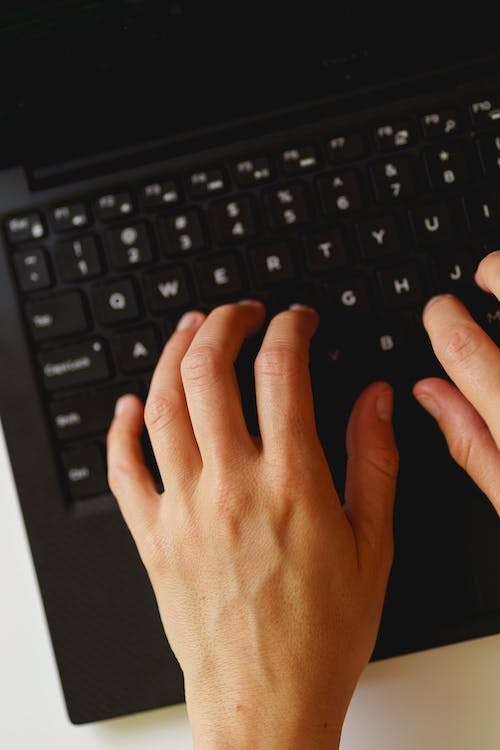 Deux mains tapant sur le clavier d'un ordinateur portable noir à un bureau blanc.