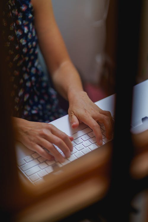 Femme tapant sur un clavier Apple Magic à une table de bureau blanche dans un bureau à domicile.