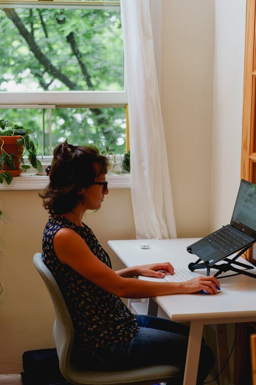 Femme travaillant de chez elle dans un bureau à domicile sur un bureau compact blanc et une chaise ergonomique ikea.
