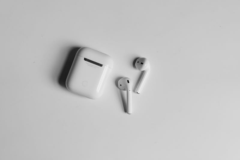Boîtier Apple Airpods et 2 AirPods sur une table blanche avec des ombres.