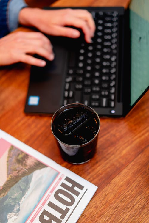 Un verre délicat rempli de café glacé à côté d'un ordinateur portable noir avec une fille qui tape sur le clavier.