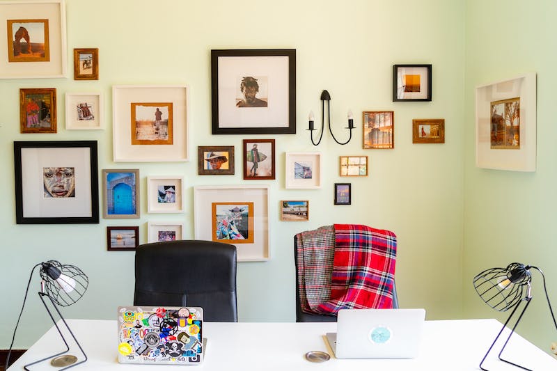 Un espace de coworking chic avec des photos encadrées au mur et un grand bureau blanc partagé avec deux ordinateurs portables et des lampes en métal noir.