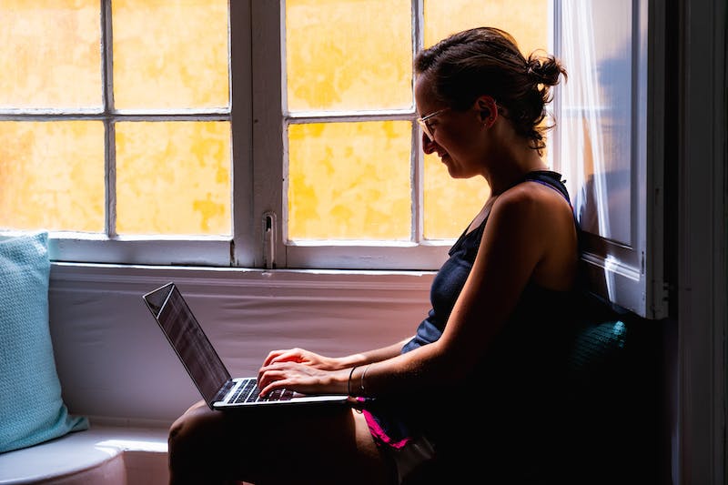 Femme assise dans un siège de fenêtre travaillant à distance à partir d'un ordinateur portable noir à Tenerife.