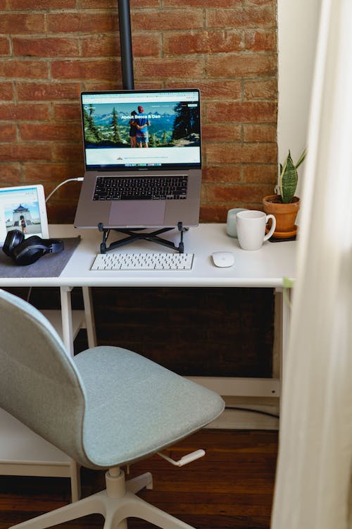 Bureau à domicile dans un petit appartement avec support pour ordinateur portable, clavier sans fil, souris sans fil, bureau de travail blanc et chaise de bureau blanche et verte.
