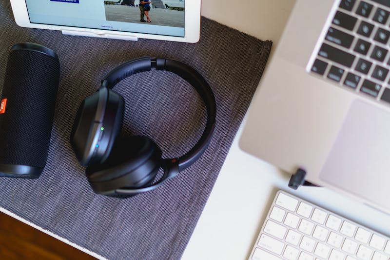 Casque bluetooth sans fil, haut-parleur bluetooth compact noir et ordinateur portable avec clavier sans fil sur un set de table gris sur un bureau blanc.