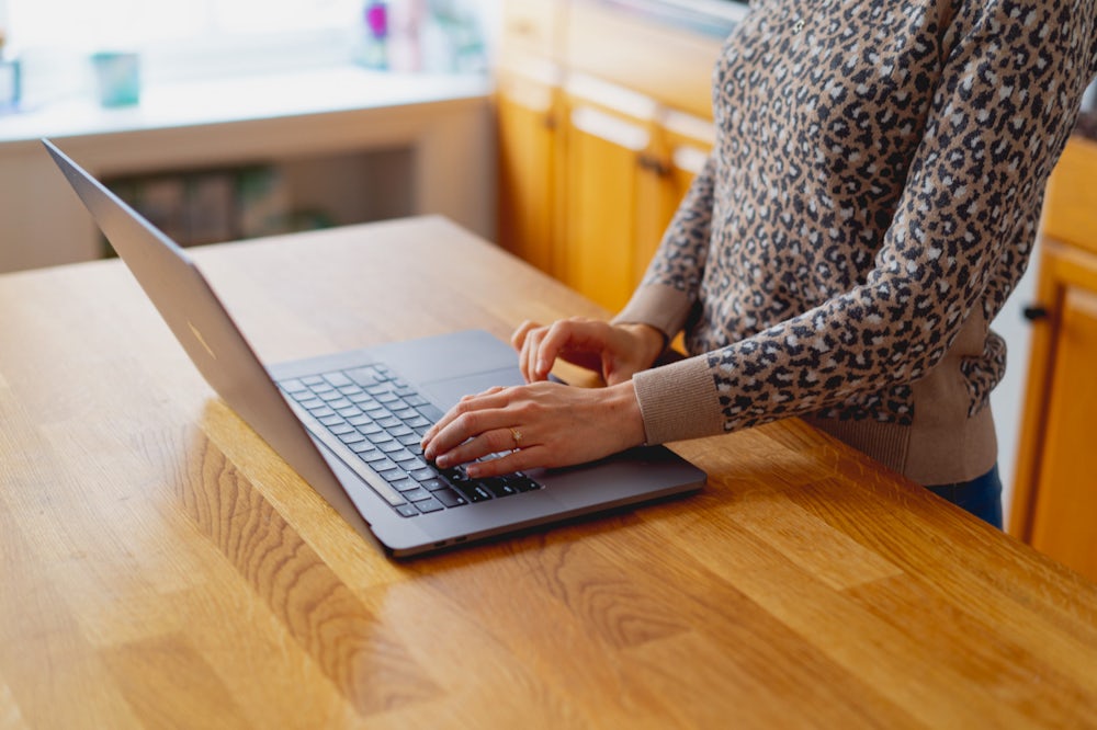 Main de femme utilisant un MacBook Pro de 16 pouces sur un comptoir en bois