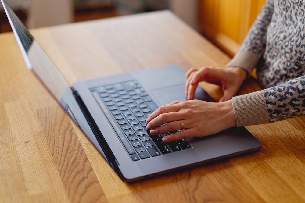 Main de femme utilisant un MacBook Pro 16 pouces sur un comptoir en bois