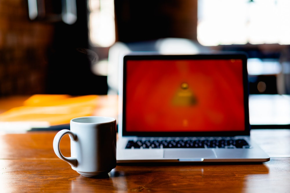 Tasse à café blanche à côté d'un MacBook Pro sur une table de bureau en bois dans un espace de coworking.