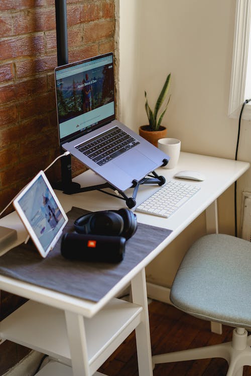 Bureau à domicile minimaliste dans un petit appartement avec un ordinateur portable sur un support, un mur en briques apparentes et une chaise de bureau ergonomique.