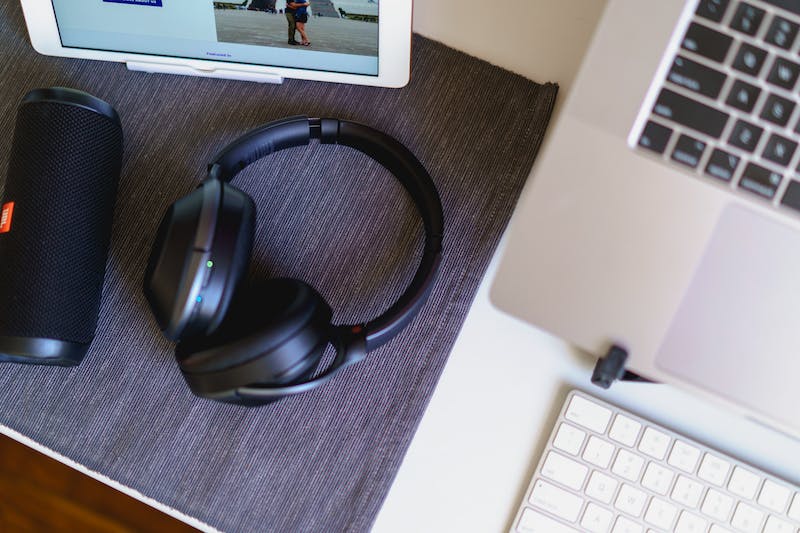 Casque bluetooth sans fil, enceinte bluetooth compacte noire et ordinateur portable avec clavier sans fil sur un set de table gris sur un bureau blanc.